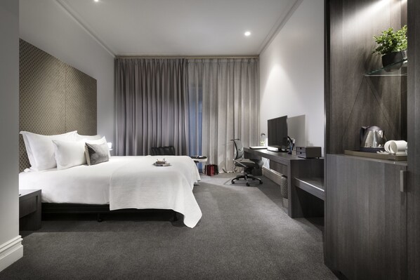 Une chambre d’hôtel moderne avec un grand lit, un bureau équipé d’un ordinateur, une télévision et une petite plante.