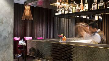 Zona de bar con diseño moderno, destacando un muro con patrón, diversidad de botellas de licor y taburetes de bar.