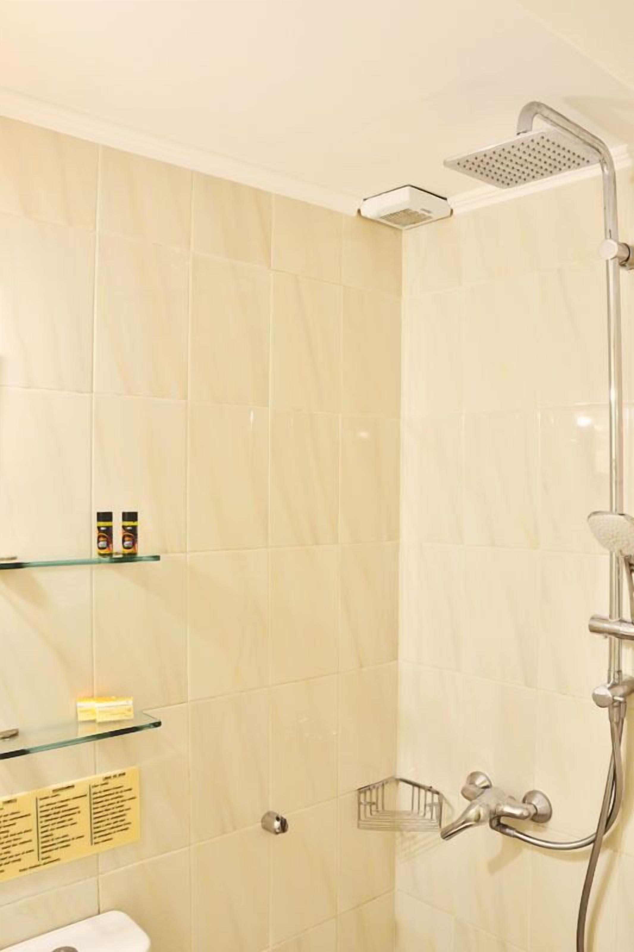 Un baño con ducha, un estante de vidrio con artículos de aseo y un perchero para toallas.