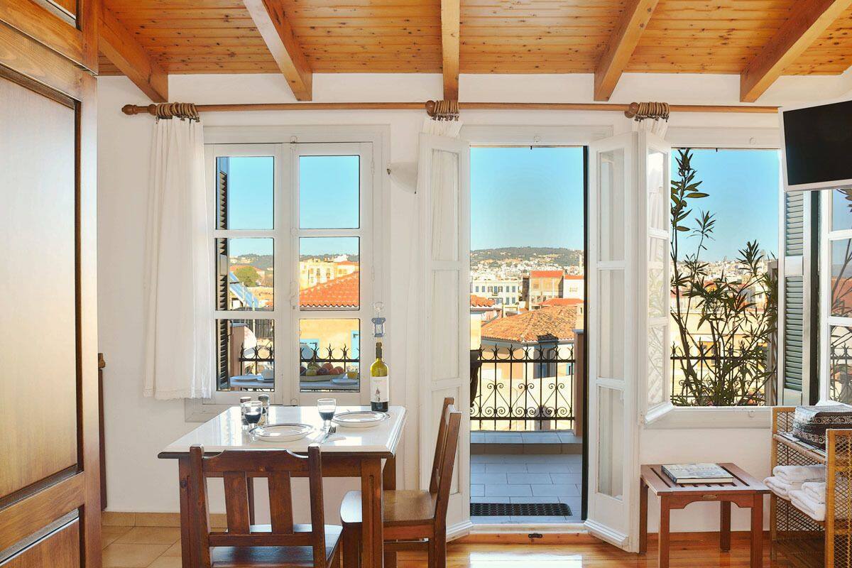 Uma área de refeições com uma mesa posta para dois, grandes janelas com vista para um horizonte urbano e uma varanda com guarda-corpo.