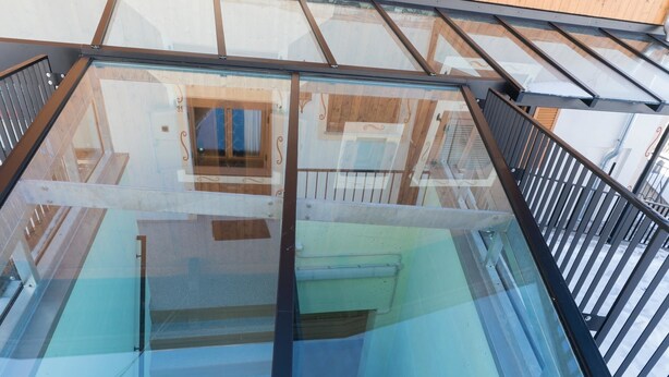 A glass-enclosed balcony with a metal railing, wooden shutters on the windows, and a clear view of the interior.