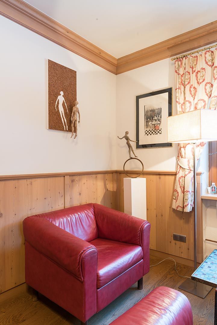 Quarto com sofá de couro vermelho, uma pequena mesa, um quadro na parede e uma janela com cortinas.