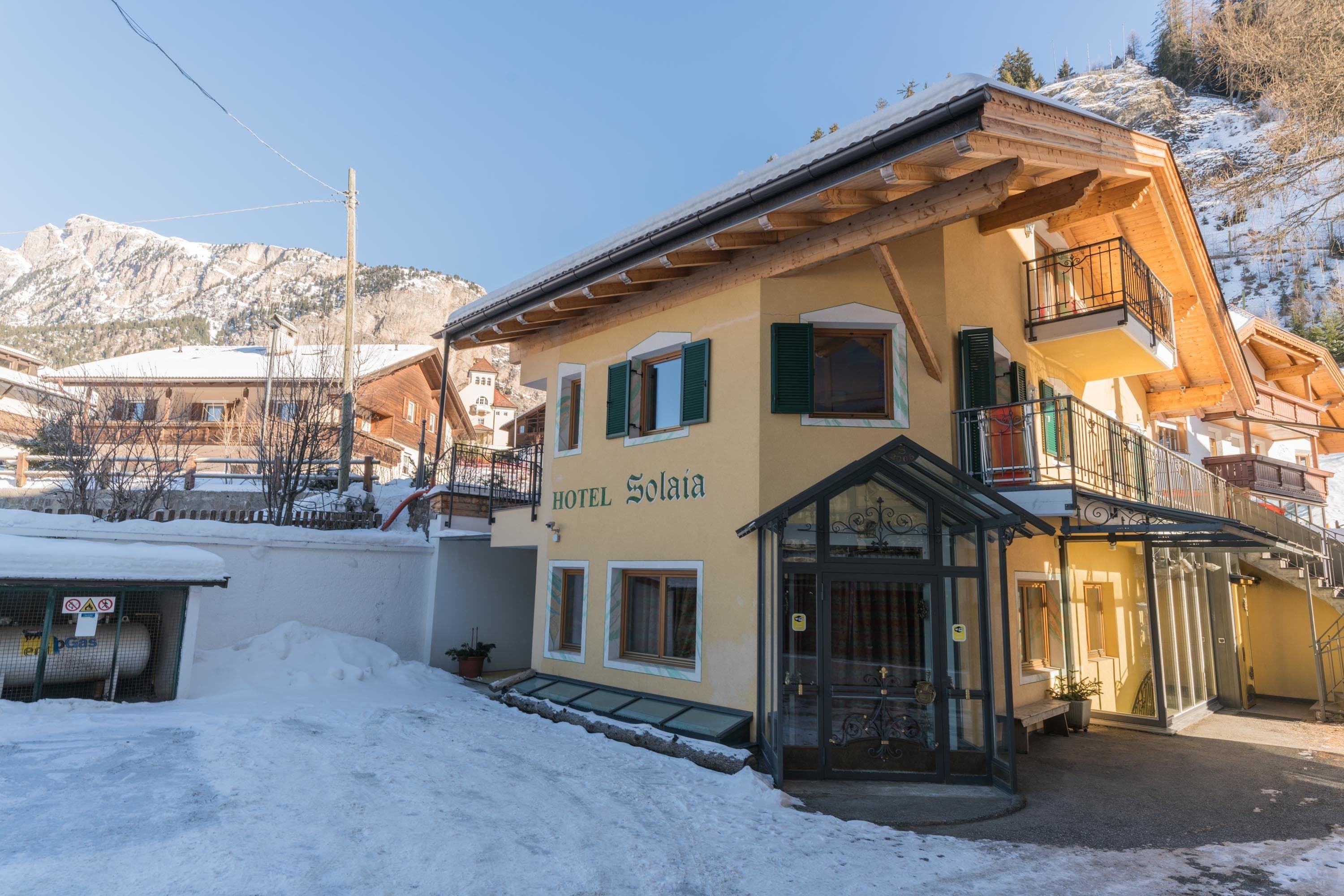 A hotel named "HOTEL Solaja" with a traditional Alpine architectural style, featuring a balcony and a glass entrance.