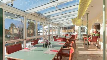Een restaurant met glazen wanden, rode stoelen en groene tafels.