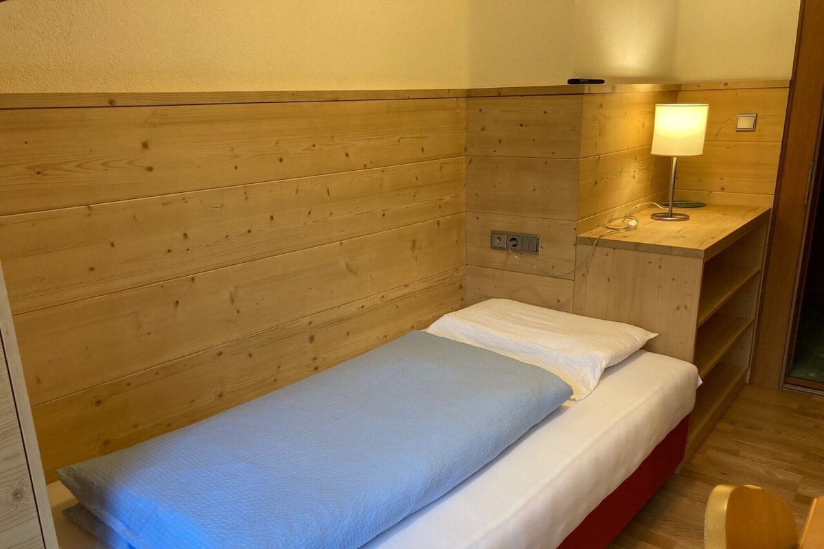 Een enkel bed met houten hoofdbord, een nachtkastje met lamp en een klein plankje.