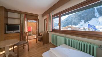 A hotel room with a bed, a desk, a chair, a TV, and a window with a view of a snowy mountain.