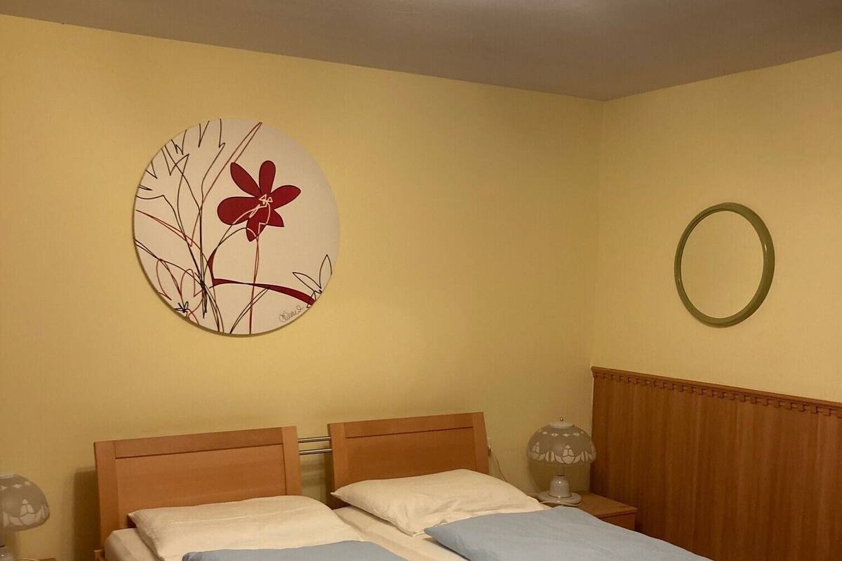 Een tweepersoonsbed met een houten hoofdeinde, een nachtkastje met een lamp, en een decoratie aan de muur.