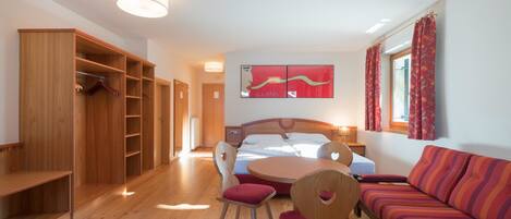 A bedroom with a bed, a wooden wardrobe, a round table with chairs, and a sofa.
