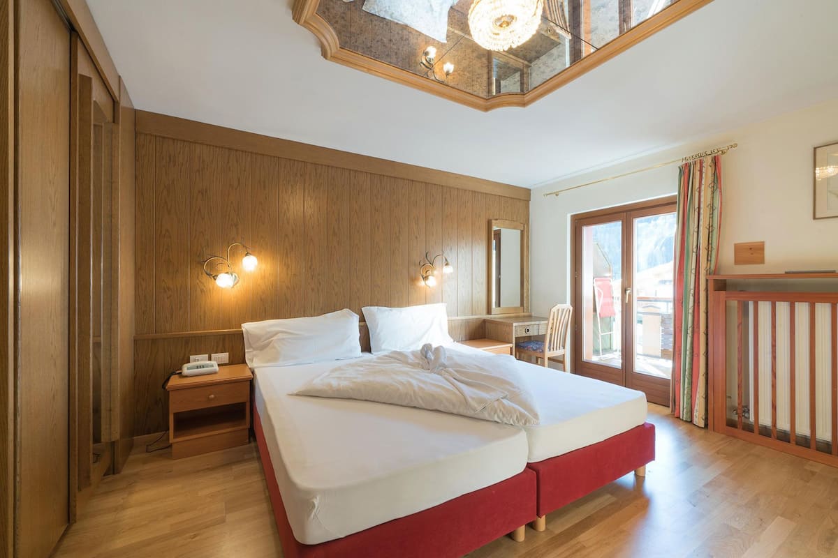 Een slaapkamer met een houten paneelwand, een bed met wit beddengoed, een nachtkastje, een spiegel en een raam met gordijnen.
