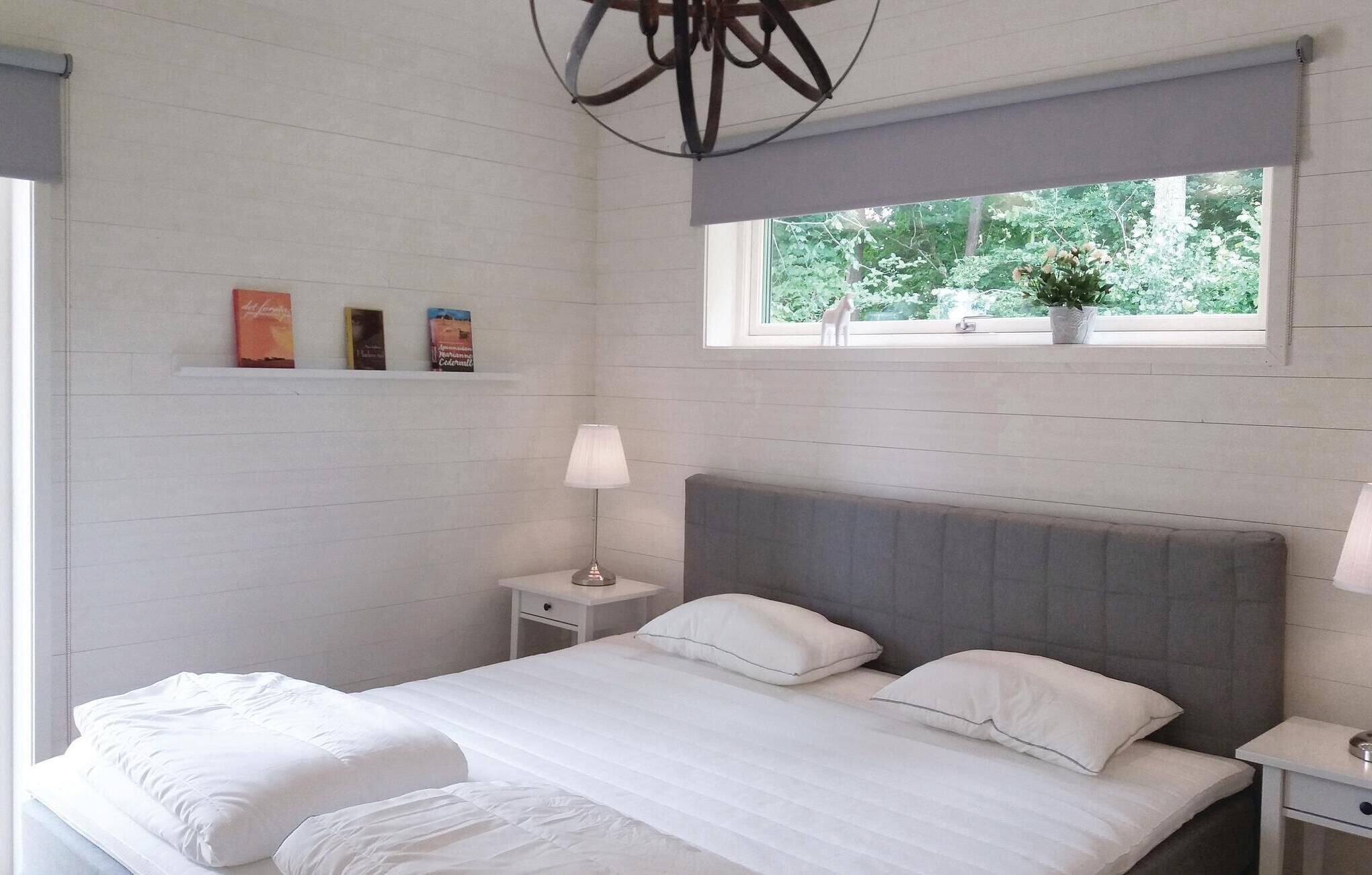 Un dormitorio con cama, mesitas de noche, ventana con vistas a zonas verdes y estante con libros.