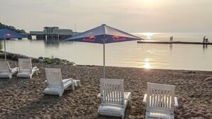 Une plage avec des chaises longues blanches et un parasol.
