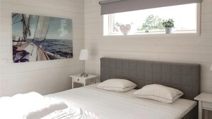 Une chambre à coucher comprenant un lit, une table de chevet, une lampe, une fenêtre avec vue et un tableau accroché au mur.