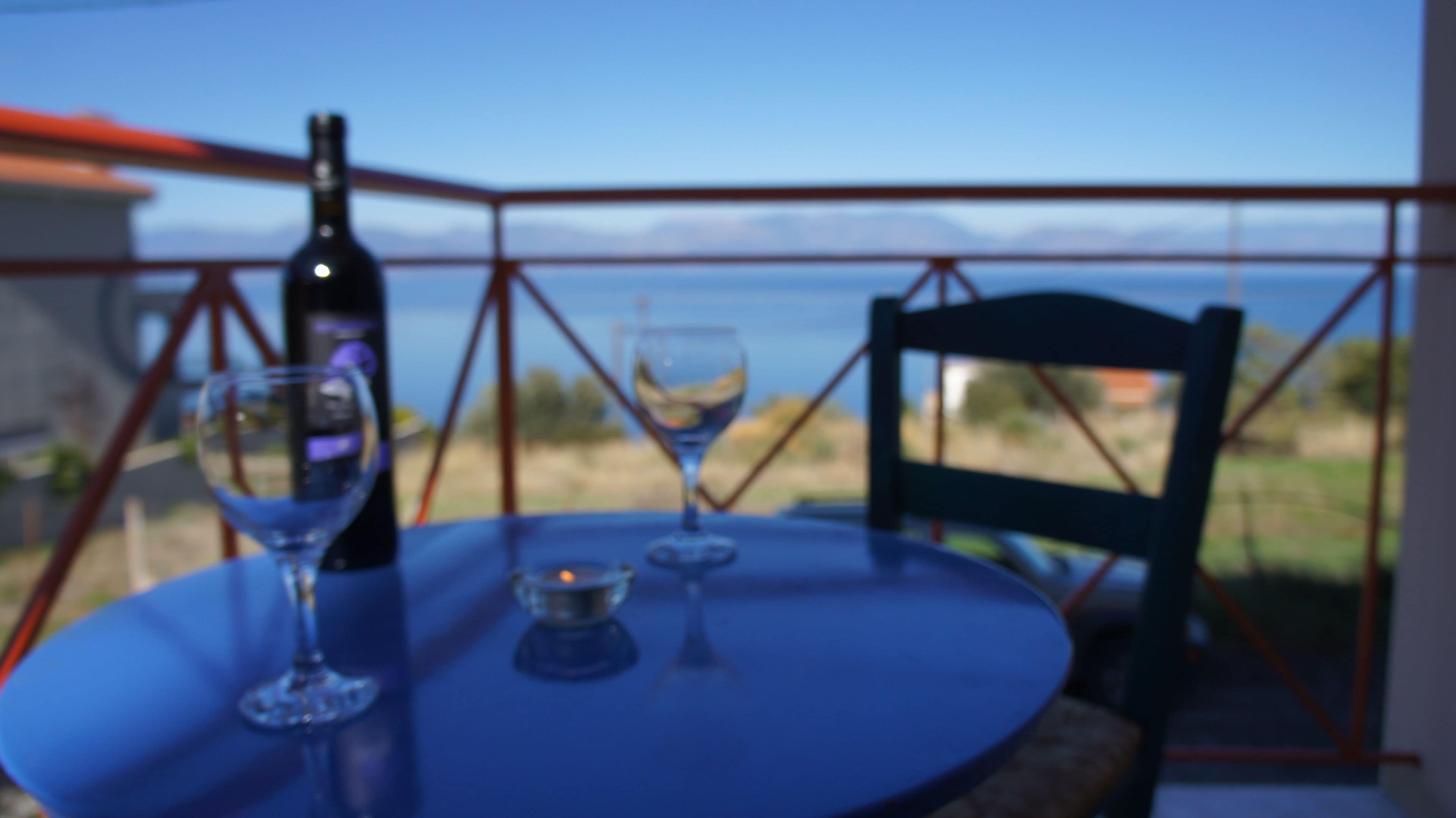Une table avec une bouteille et deux verres, placée devant un paysage de montagnes et une rambarde rouge.