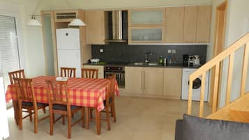 A compact kitchen with wooden cabinets, a dining table with chairs, a built-in oven, and a washing machine.