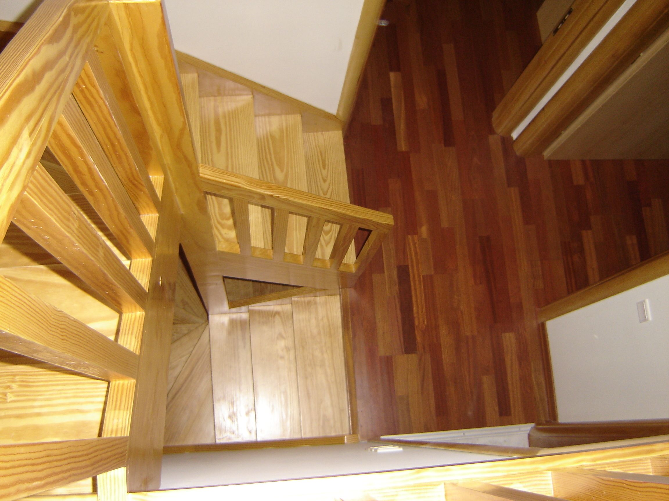A wooden staircase with a wooden railing, leading to a room with wooden flooring.