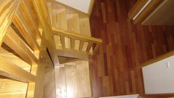 A wooden staircase with a wooden railing, leading to a room with wooden flooring.