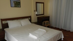 Una cama bien hecha con sábanas blancas, un cabecero de madera, una mesita de noche de madera, un espejo y un cuadro en la pared.