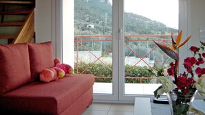 Una habitación con un sofá rojo, una mesa de vidrio con un jarrón de flores y vistas a un paisaje montañoso a través de un ventanal grande.