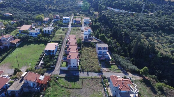 An aerial view of a residential area with houses arranged in a grid pattern, surrounded by greenery and hills. - Stavento - Villas Trapeza & Voura (Aigialeia)