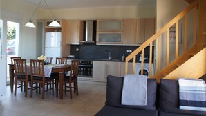 Cocina compacta con armarios de madera, una mesa de comedor con sillas y una escalera que sube a un altillo.