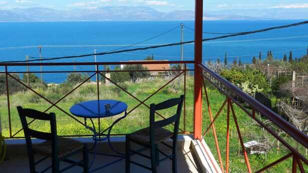 Un balcón con mesa y sillas que da a un paisaje costero con montañas al fondo.