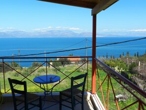 A balcony with a table and chairs overlooking a coastal landscape with mountains in the distance. - Stavento - Villas Trapeza & Voura (Aigialeia)