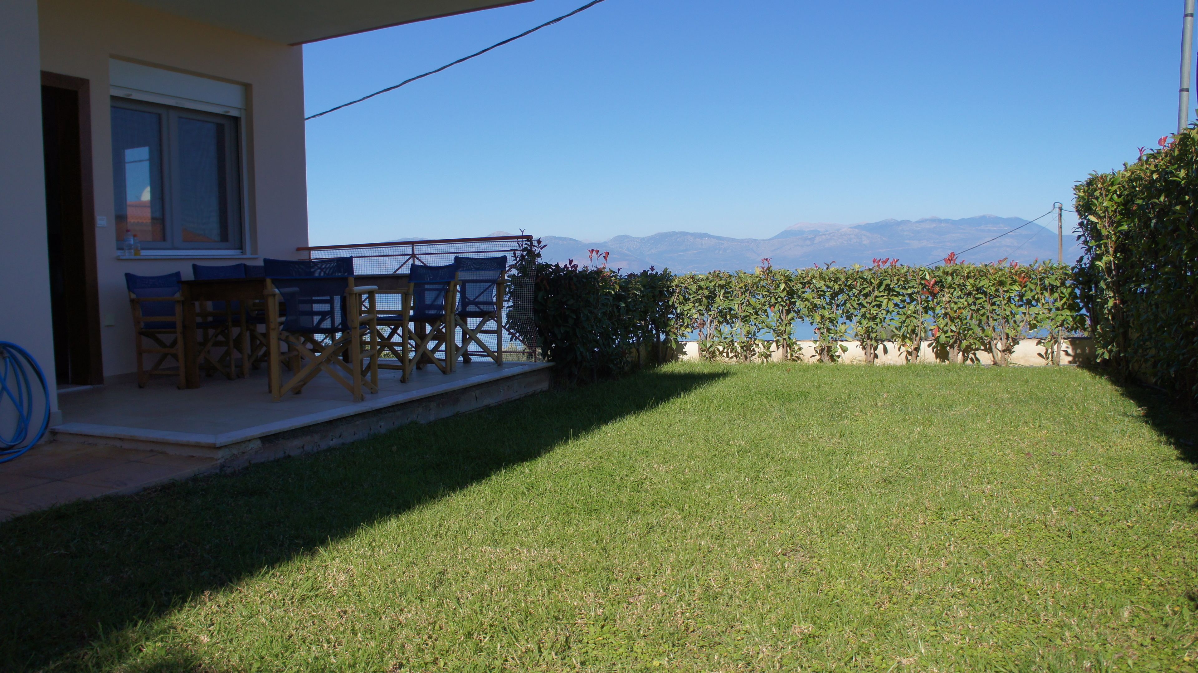 A patio with a table and chairs, a grassy lawn, and a view of mountains.
