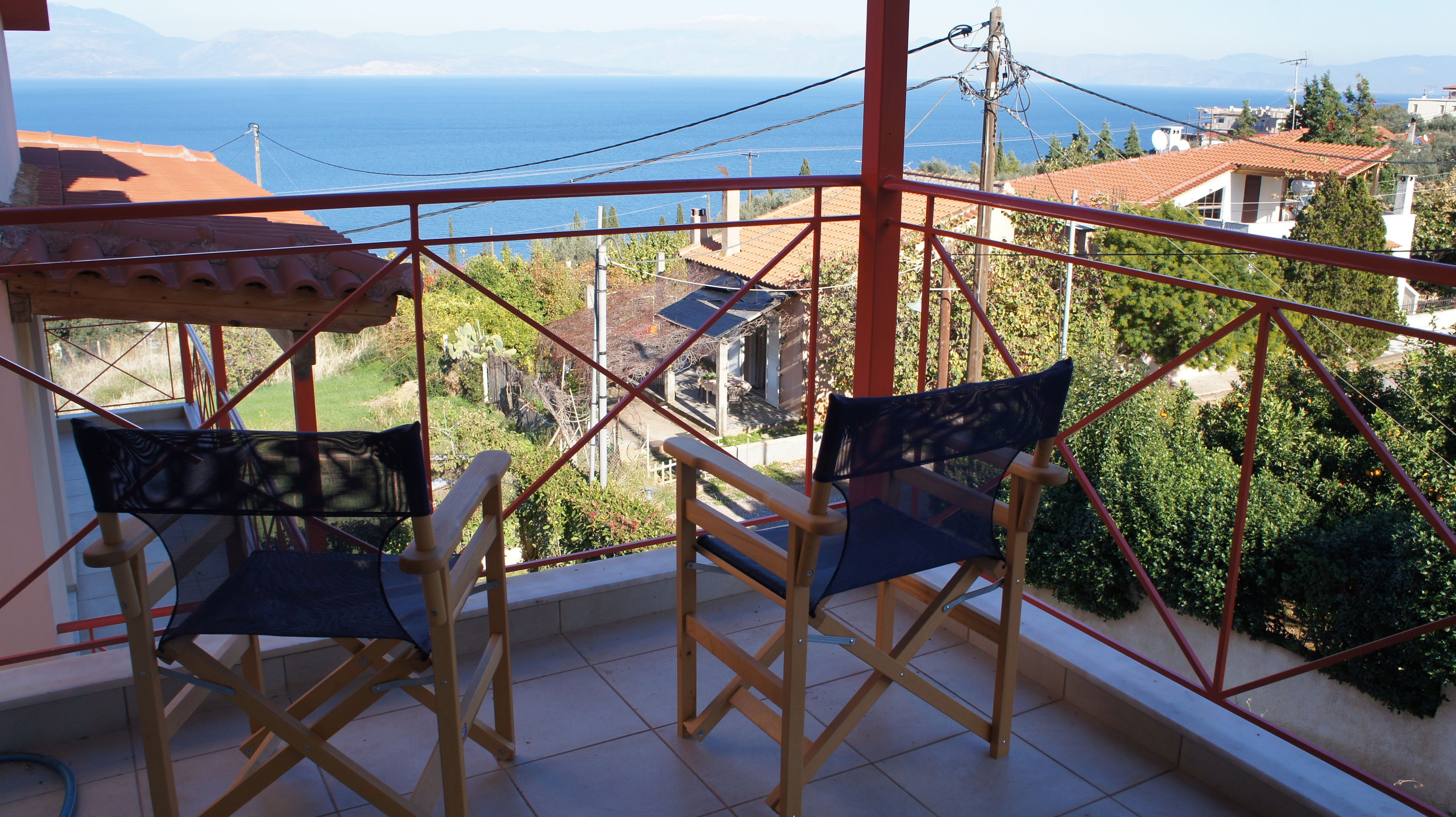Un balcon avec deux chaises et une table, offrant une vue sur la côte, avec des maisons et de la verdure.