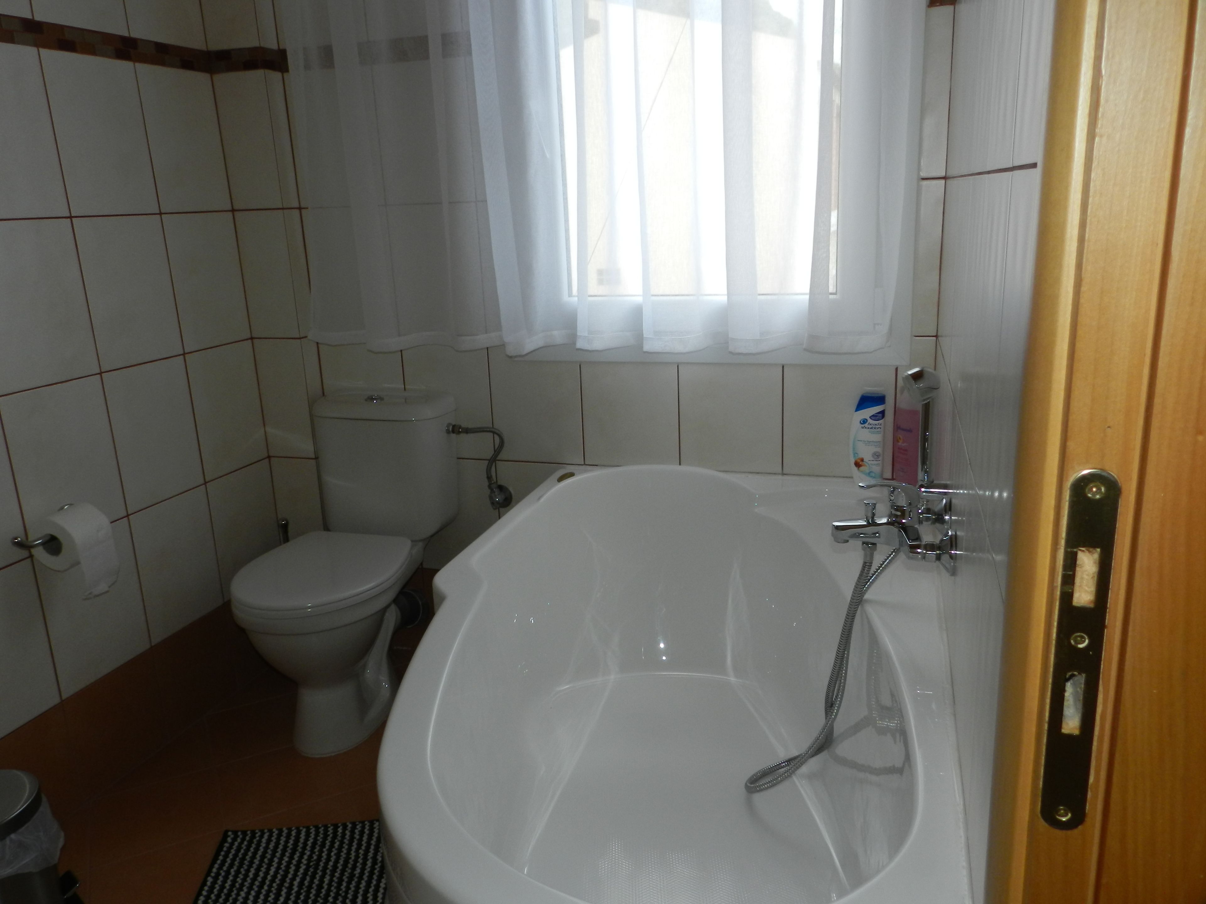 A bathroom with a toilet, a bathtub, and a window with curtains.