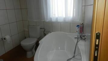 A bathroom with a toilet, a bathtub, and a window with curtains.