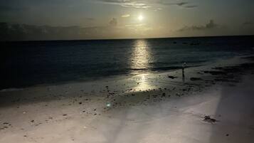 Una playa de noche con el reflejo de la luna visible en el agua.