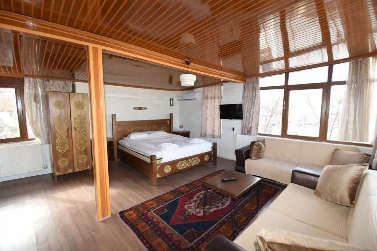 A room with a wooden ceiling, a bed, a sofa, a TV, and a window.