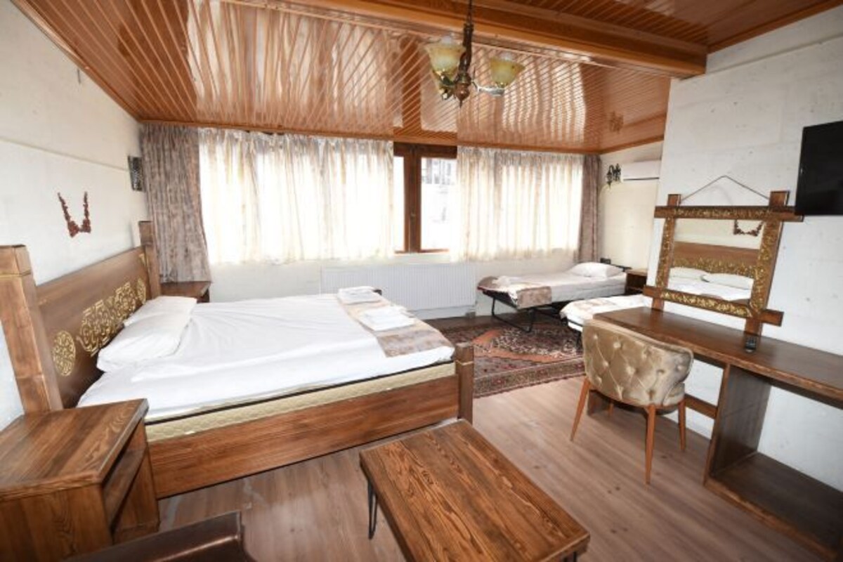 A room with two beds, a desk, a chair, a TV, and a window with curtains.