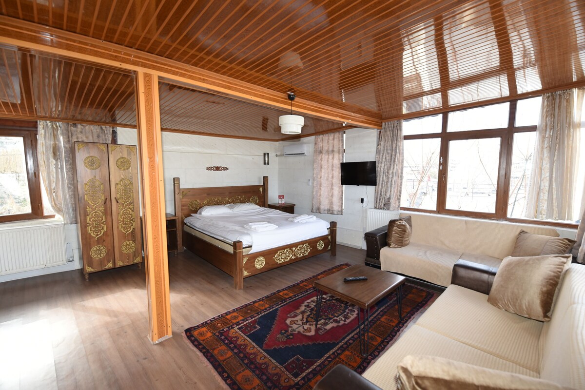 A room with a wooden ceiling, a bed, a sofa, a television, and a window.