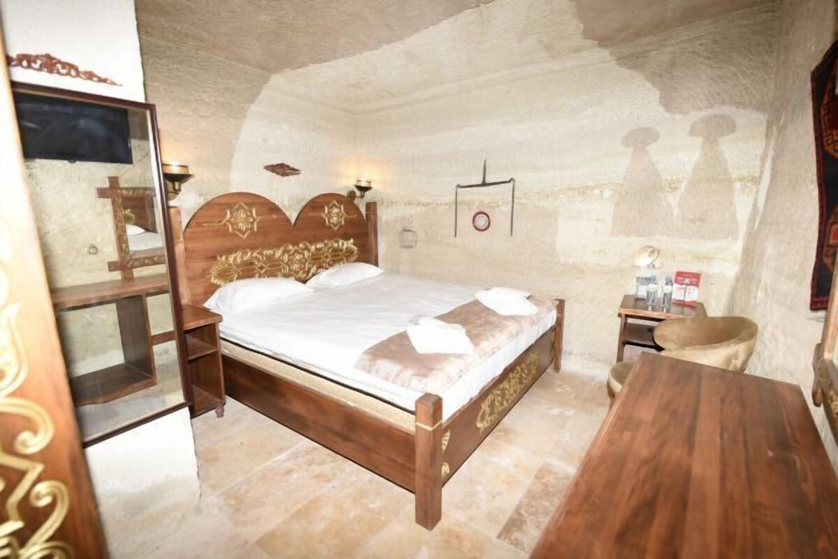A bedroom with a wooden bed, a nightstand, a mirror, and a wooden table.