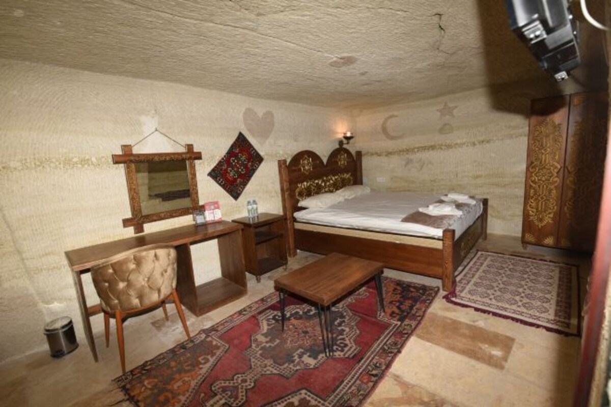 A bedroom with a bed, a desk, a chair, a mirror, and a hanging tapestry.