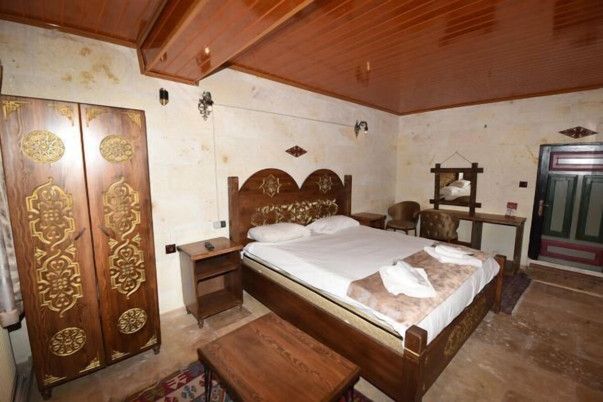 A bedroom with a wooden bed, a wardrobe with intricate designs, a bedside table, and a desk with a chair.