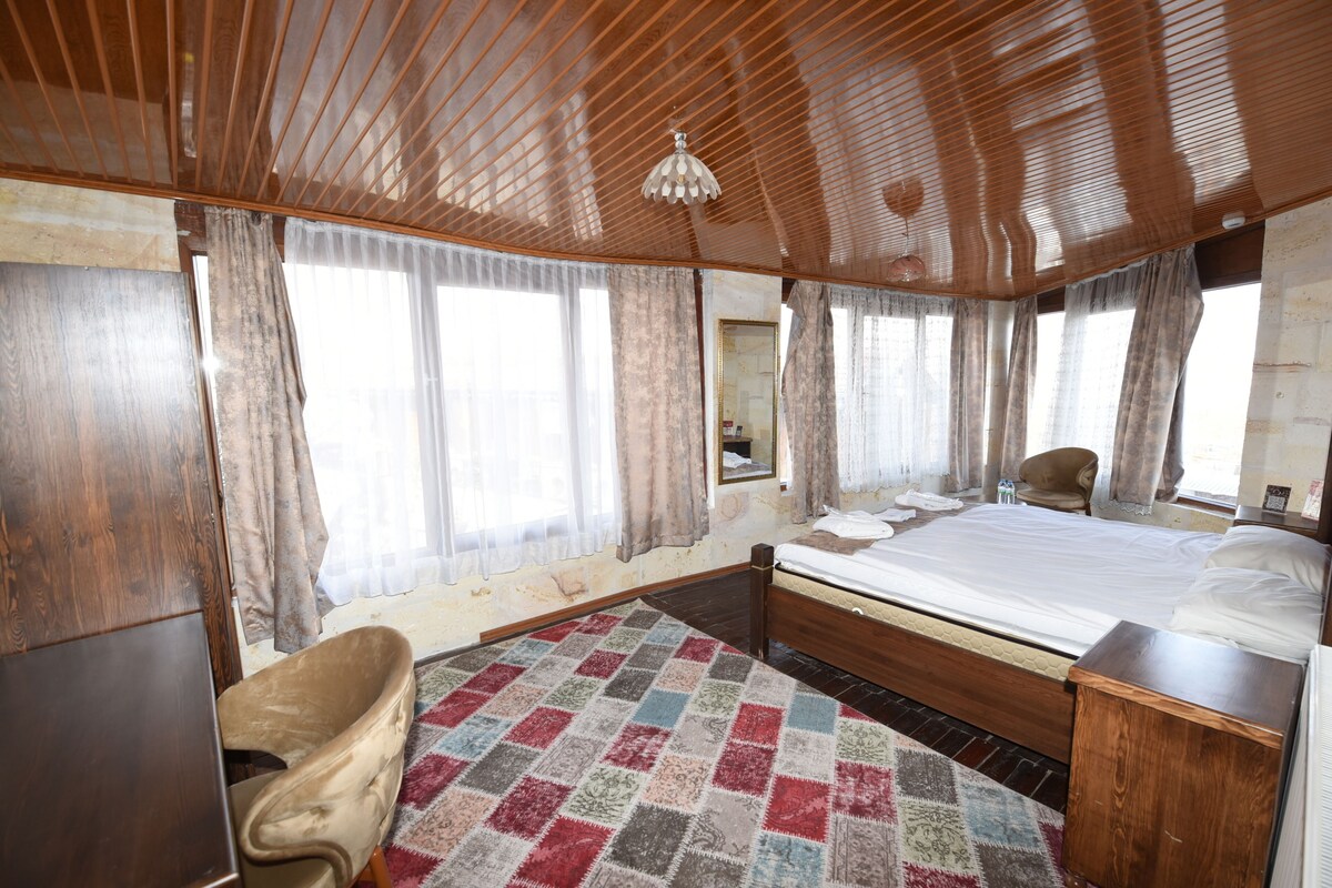 A bedroom with a wooden ceiling, a bed, a chair, a rug, and a window with curtains.