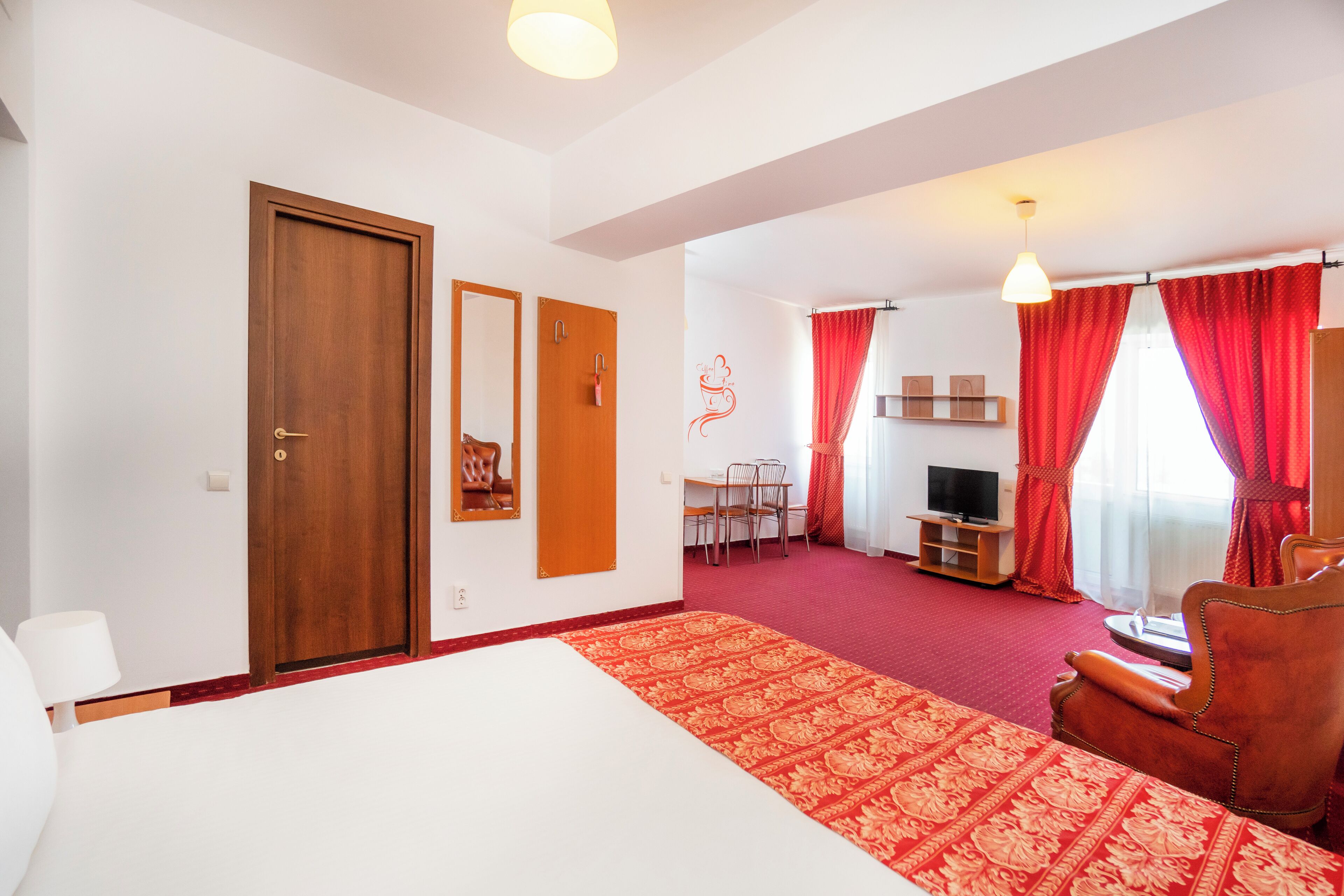 A hotel room with a large bed, a desk with a chair, a TV, and red curtains.