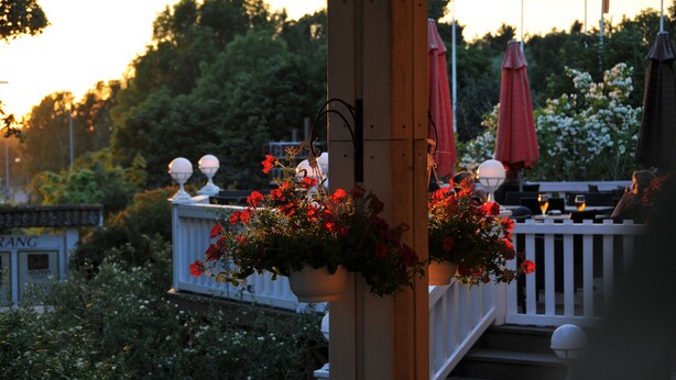 Una terraza de madera con barandillas blancas y macetas de flores rojas.