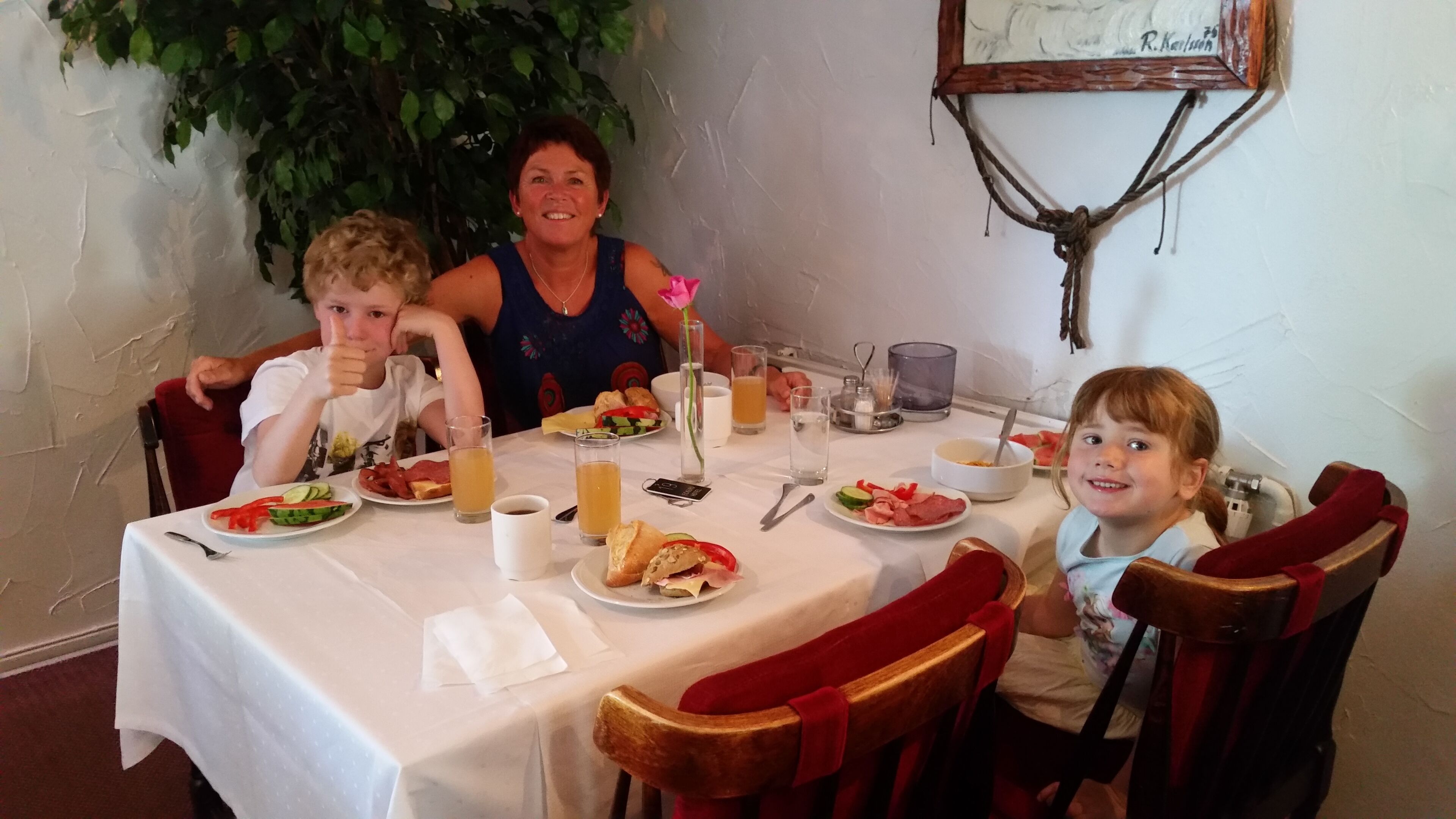A dining table with plates of food, glasses, and a vase with a flower.