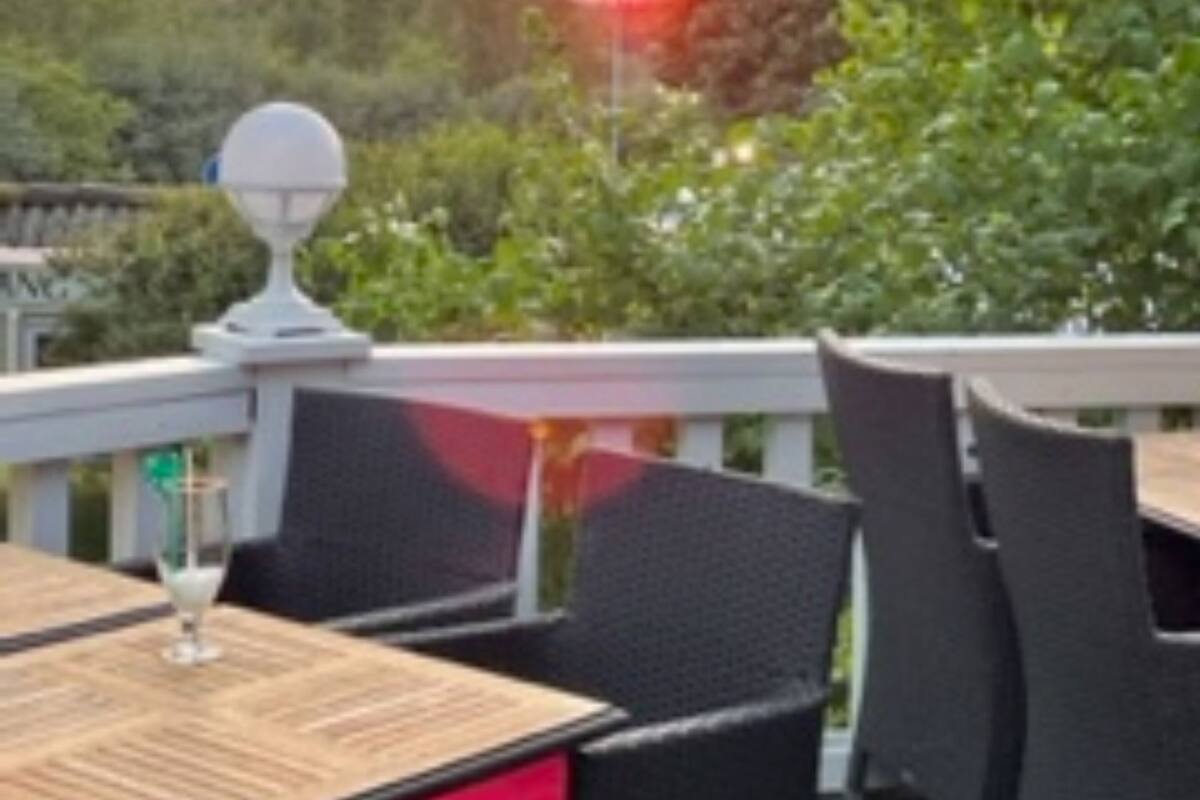 An outdoor patio with wicker furniture and a table with a red cushion.