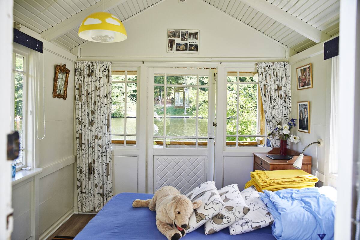 A cozy bedroom with a bed, a teddy bear, and a view of greenery outside.