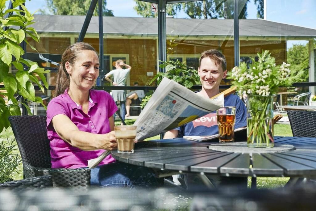 Two people sitting at an outdoor table with a newspaper, a glass of beer, and a coffee cup.