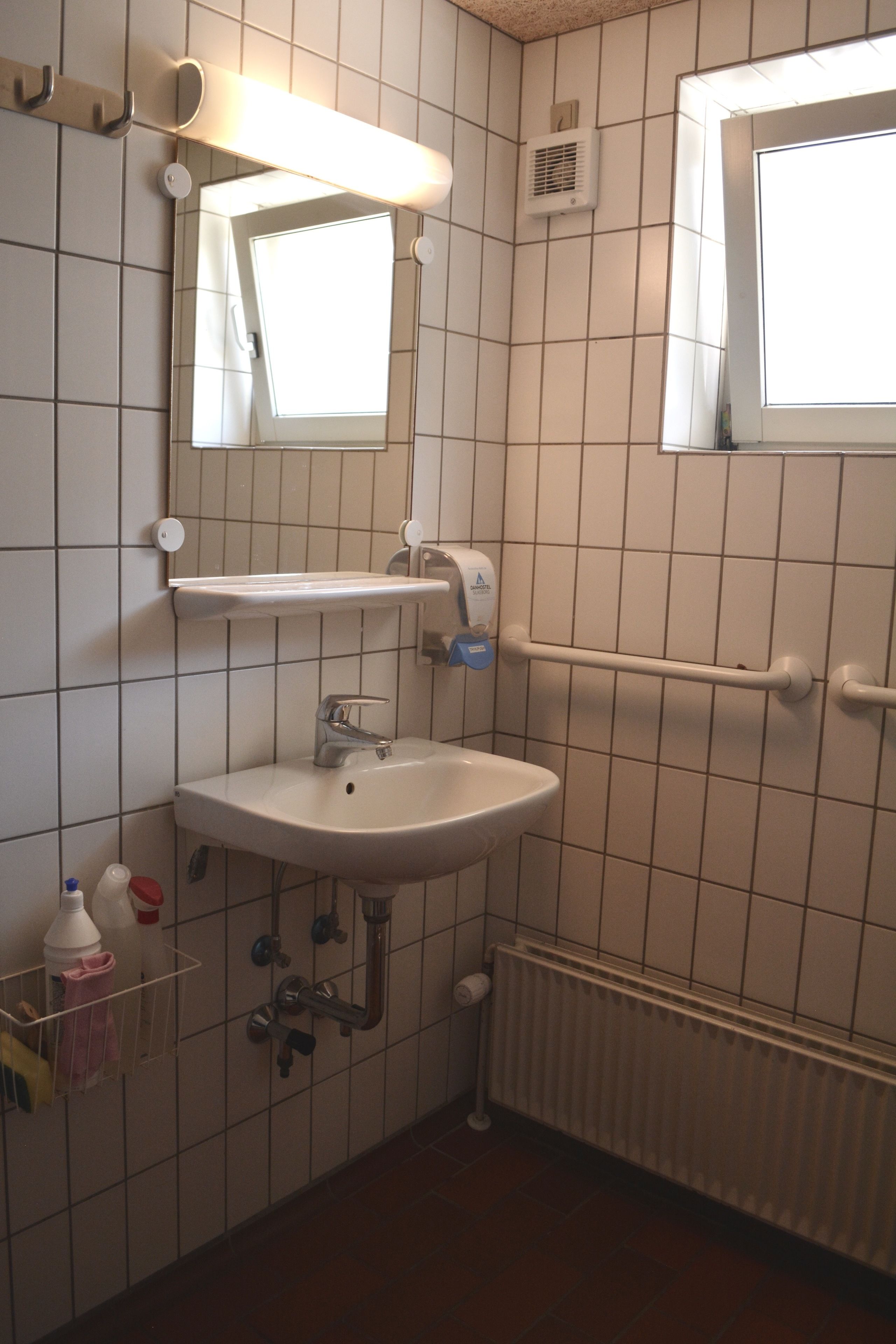 Un baño con lavamanos, espejo y secamanos.