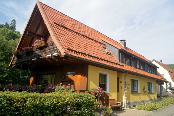 A yellow building with a red-tiled roof, a wooden balcony with flowers, and a sign reading "Hotel Bader".