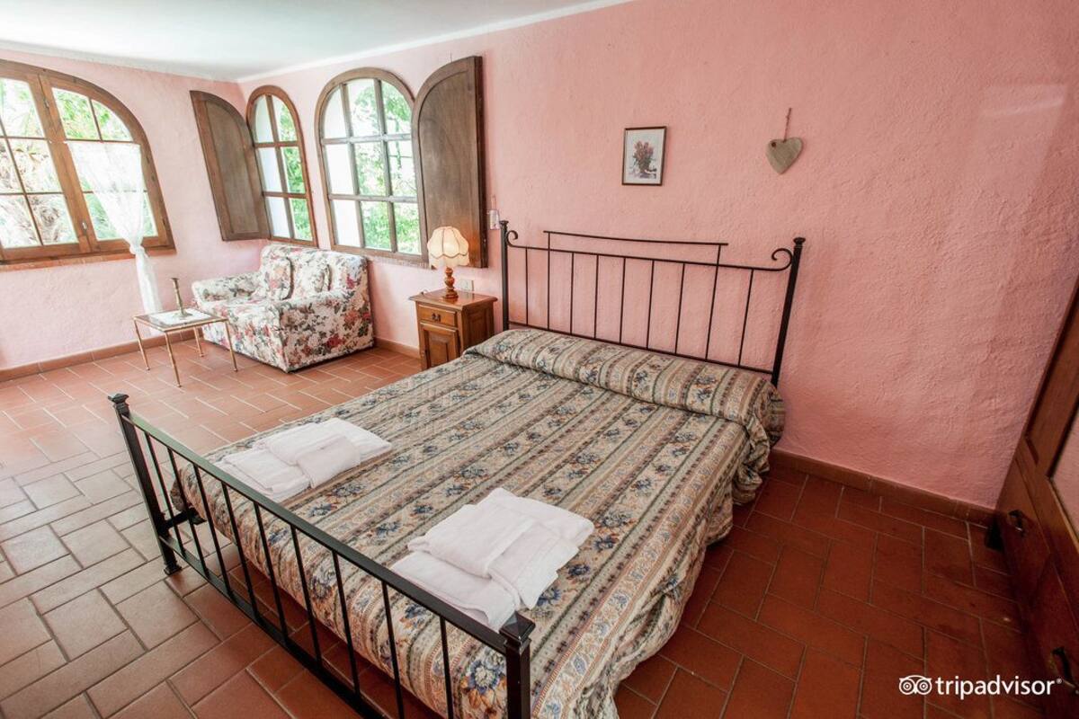Ein Schlafzimmer mit Bett, Sessel, Nachttisch und einem Fenster mit Blick ins Grüne.