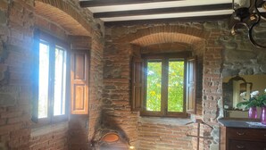A stone-walled room with a fireplace, a red sofa, and a wooden dresser. - Podere San Lorenzo (Terranuova Bracciolini)
