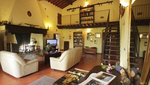 A spacious living room with a fireplace, leather sofas, a coffee table with magazines, a bookshelf, and a staircase leading to an upper level. - Podere San Lorenzo (Terranuova Bracciolini)