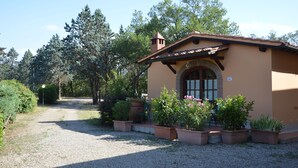 A small, single-story building with a tiled roof and a brick chimney, surrounded by a gravel path and potted plants. - Podere San Lorenzo (Terranuova Bracciolini)
